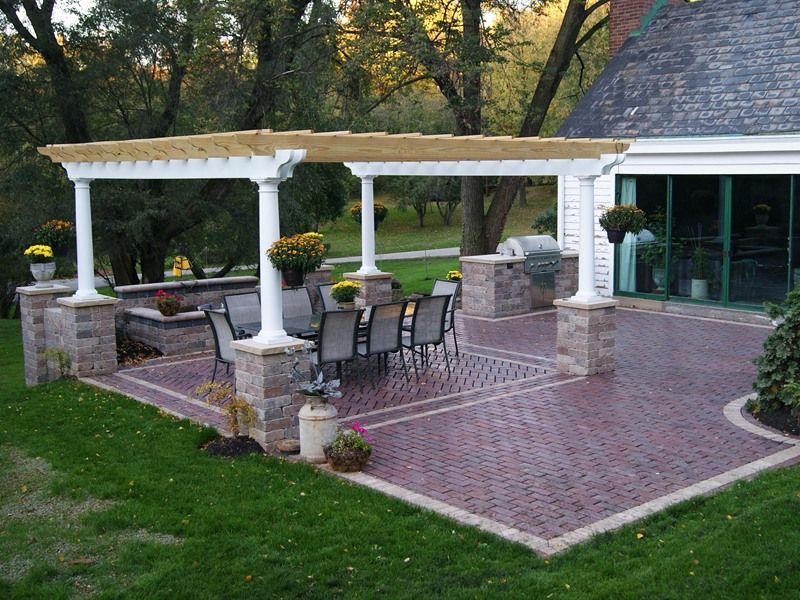 Brick patio with pergola, seating area, and outdoor grill next to a house.