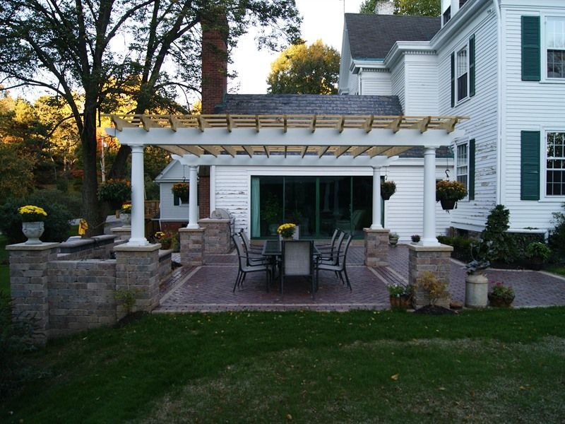 Patio with pergola, brickwork, dining set, and house in background.