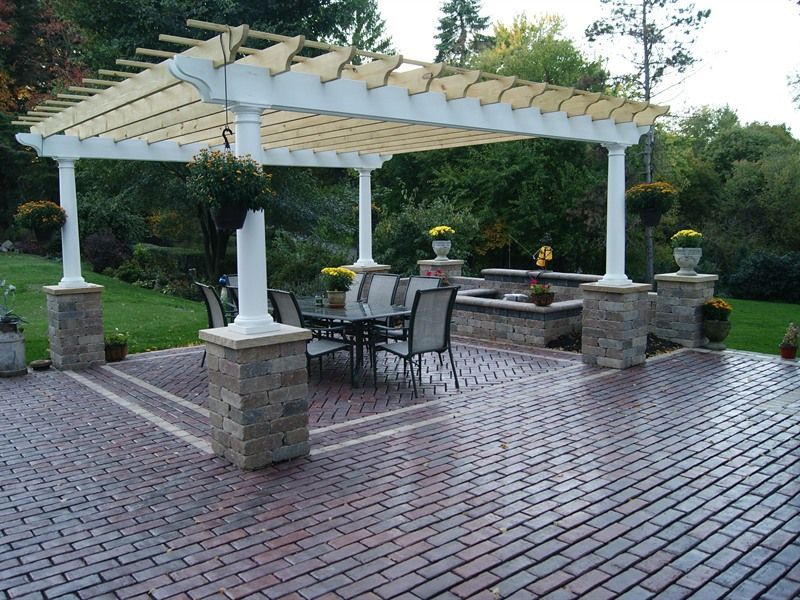 Patio with brick pavers, pergola, and outdoor dining set, surrounded by landscaping.
