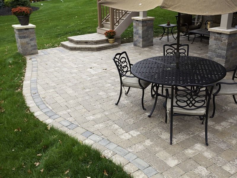 Outdoor patio with brick pavers, round table, chairs, and umbrella. Green grass surrounds.