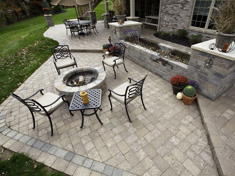 Patio with fire pit, seating, stone wall and water feature, on paved surface.