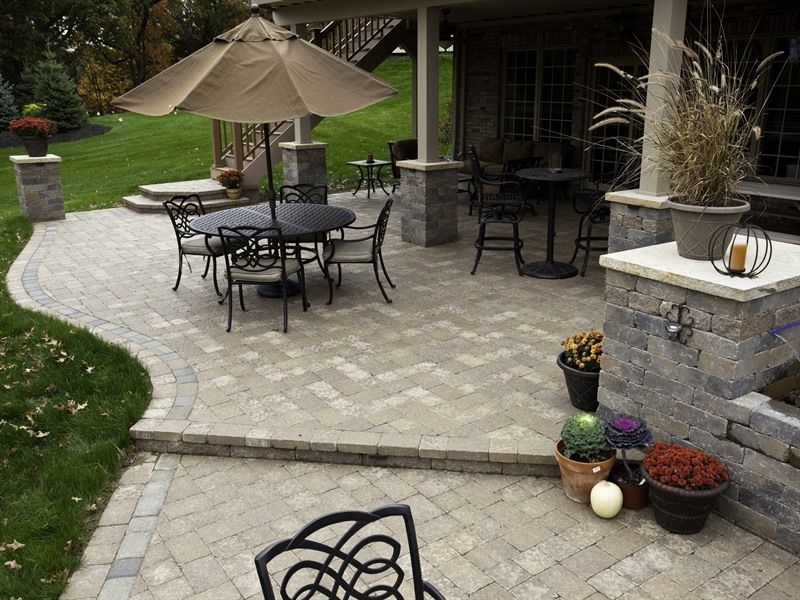 Patio with brick pavers, round table, chairs, umbrella, plants, and a partially covered seating area.