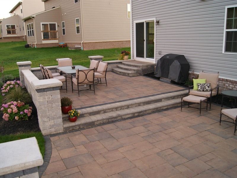 Patio with dining table, chairs, and built-in wall, steps leading to house with sliding door and grill.