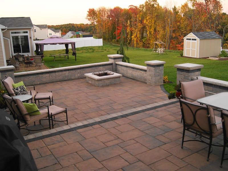 Patio with fire pit, seating, and a shed, surrounded by grass and autumn trees.