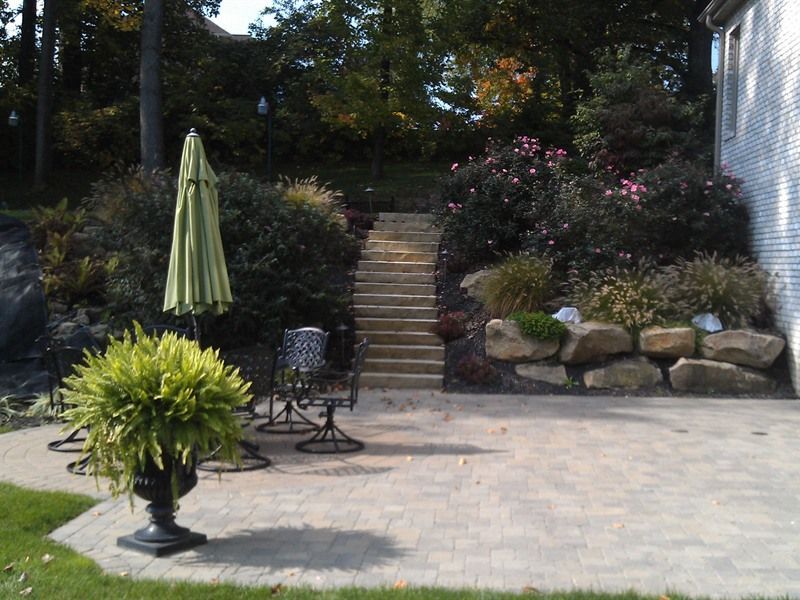 Patio with stone steps leading up to lush landscaping. Green umbrella and potted fern.