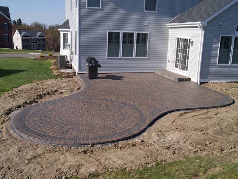 Brick patio with a curved edge and a dark circular design near a house.