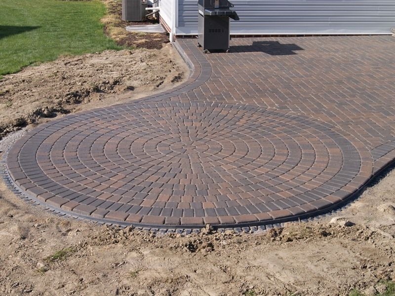 Brick patio with circular design, bordered by darker bricks, in a yard.