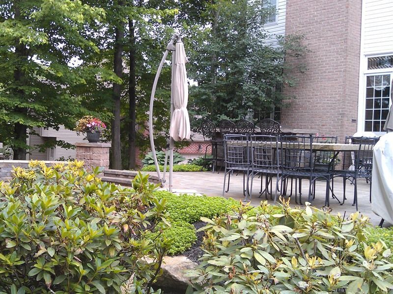 Backyard patio with table and chairs, surrounded by greenery and a brick building.
