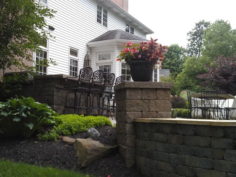 Stone patio with black bar stools, a flower pot, and a white house in the background.