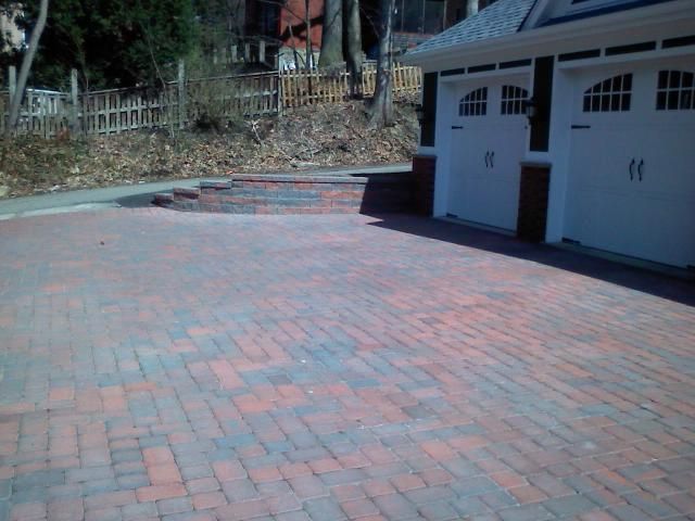Brick driveway in front of a white garage with black doors.