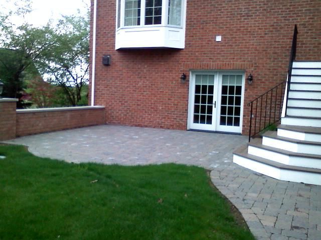 Brick patio and house with white doors, staircase, and grass.
