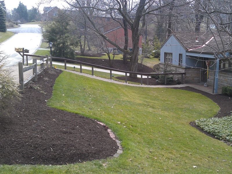 Lawn with fresh mulch border, small building, and road lined with trees. Sunny, daytime setting.
