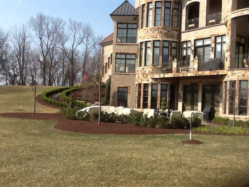 Large stone house exterior with manicured landscaping, shrubs, and grass.
