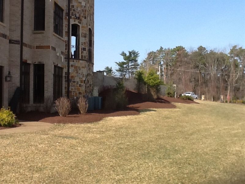 Stone building next to lawn and flower beds with a car driving in the distance.