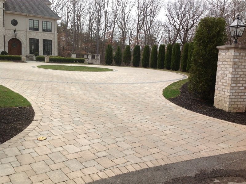 Brick paver driveway leading to a large house with a circular turn-around, surrounded by landscaping.