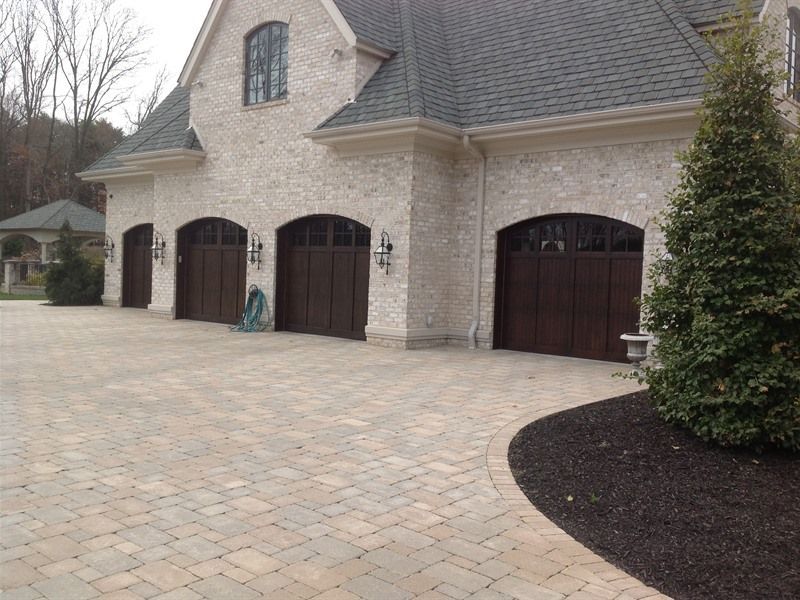 Brick home with three dark wooden garage doors, paved driveway, and landscaping.