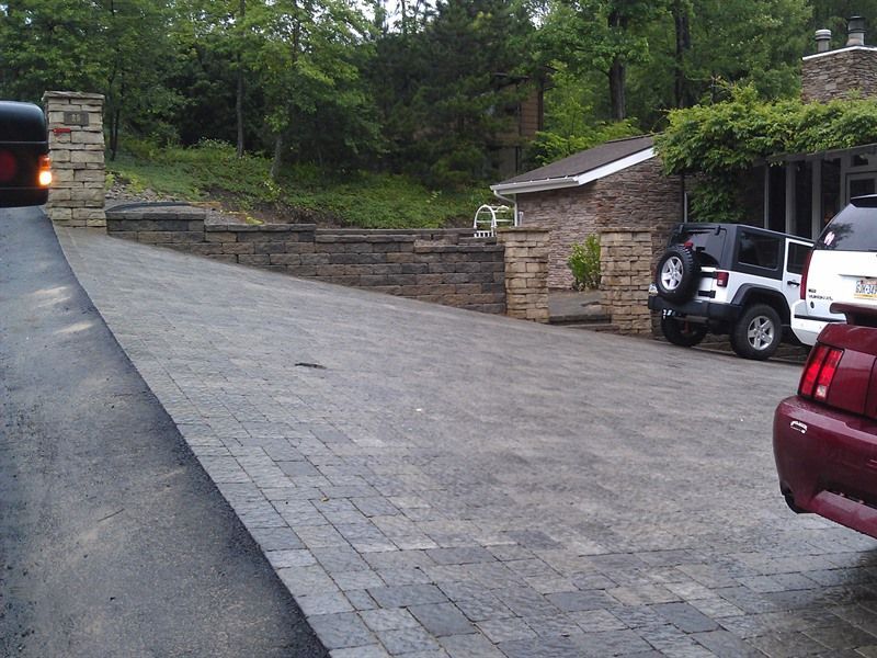 Brick driveway with retaining wall and two cars parked nearby.
