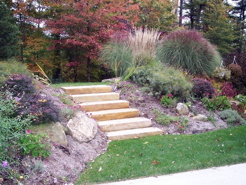 Stone steps ascend a terraced garden bed, filled with colorful autumn foliage and ornamental grasses.