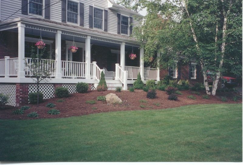 Two-story house with a porch. Landscaped front yard with a lawn, trees, and shrubs.