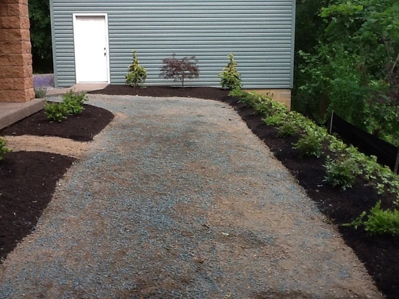 Gravel driveway with mulch borders and small plants leading to a white door in a green metal building.