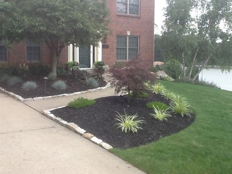 Brick house with landscaped front yard, dark mulch beds, trees, and walkway.