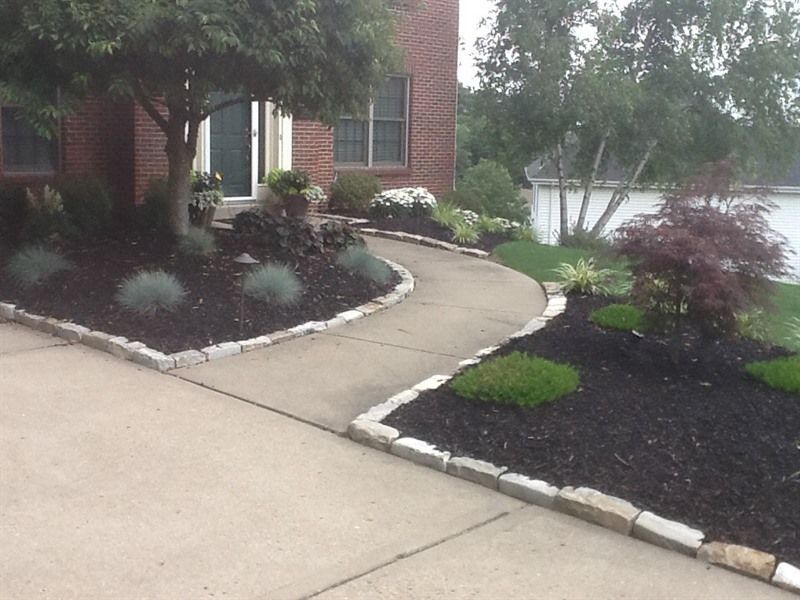 Concrete pathway curves through a landscaped yard with dark mulch and bordering stone.