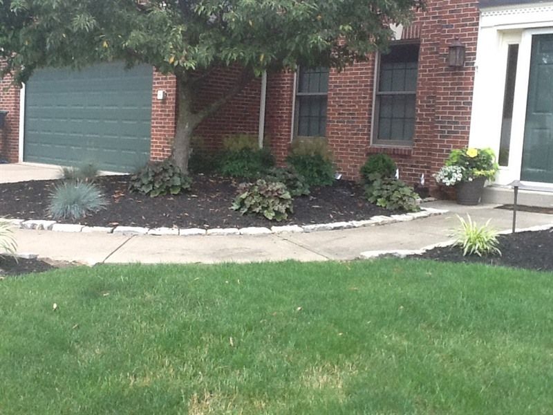 A brick house with a green garage door and dark mulch flower beds along a sidewalk.