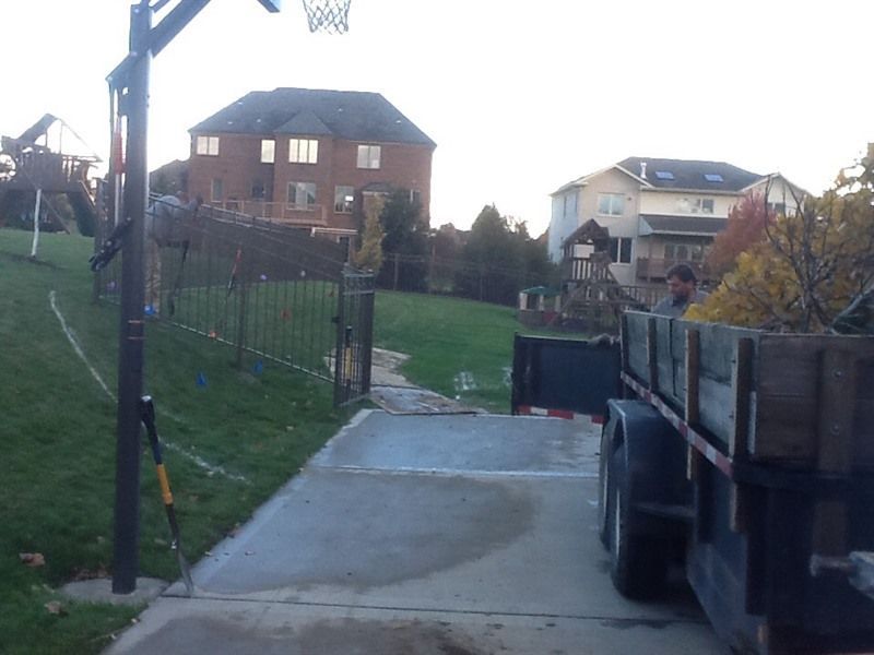 A view of a backyard with a basketball hoop, fence, and a trailer loaded with materials.