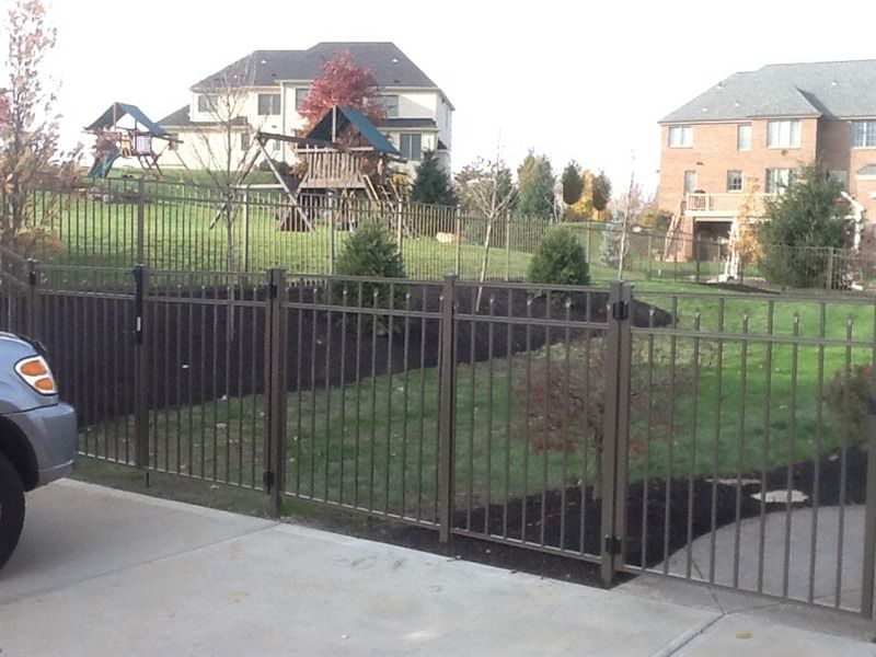Brown metal fence surrounding a backyard with a swing set and houses in the background.