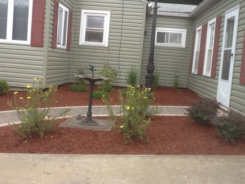 A landscaped yard with a birdbath, a path, flowers, and a house with green siding and red shutters.