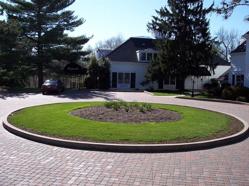 Circular brick driveway with grassy island, leading to a white building.