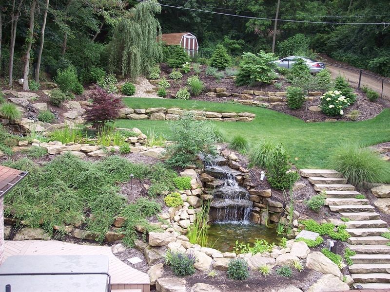 A multi-tiered landscaped yard with a waterfall feature, pond, and stone steps.
