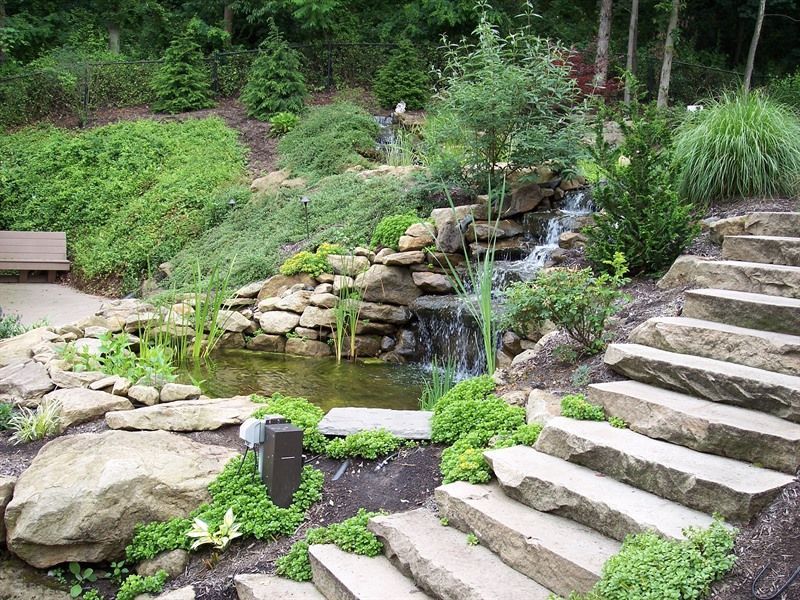 Stone steps lead up a landscaped garden with a waterfall and pond.