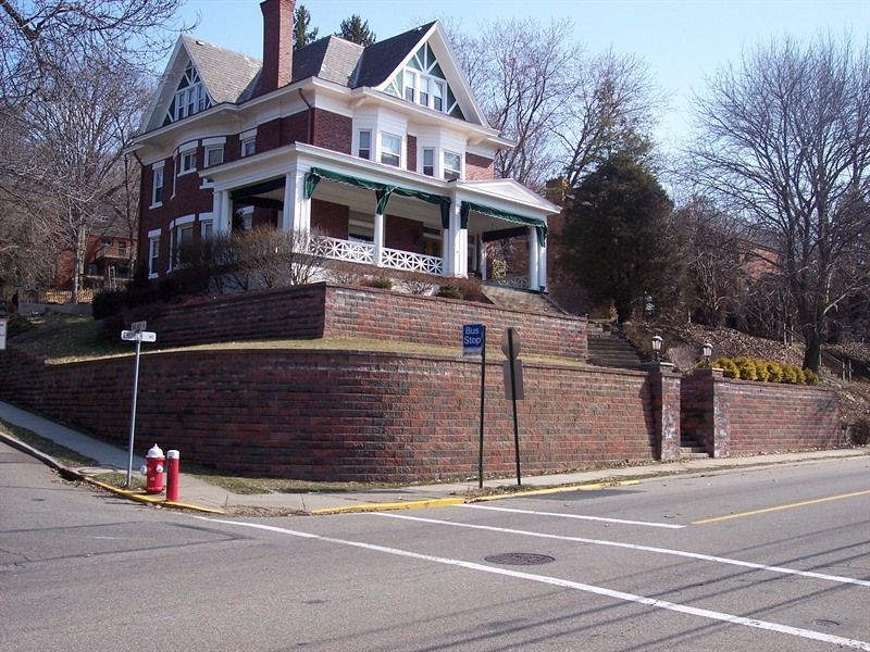 Large brick house with white trim, porch, and a retaining wall on a corner lot.