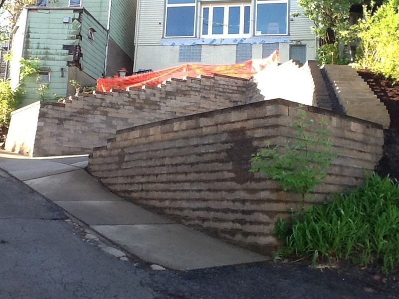 Retaining walls and staircase lead to a house on a sloped street.