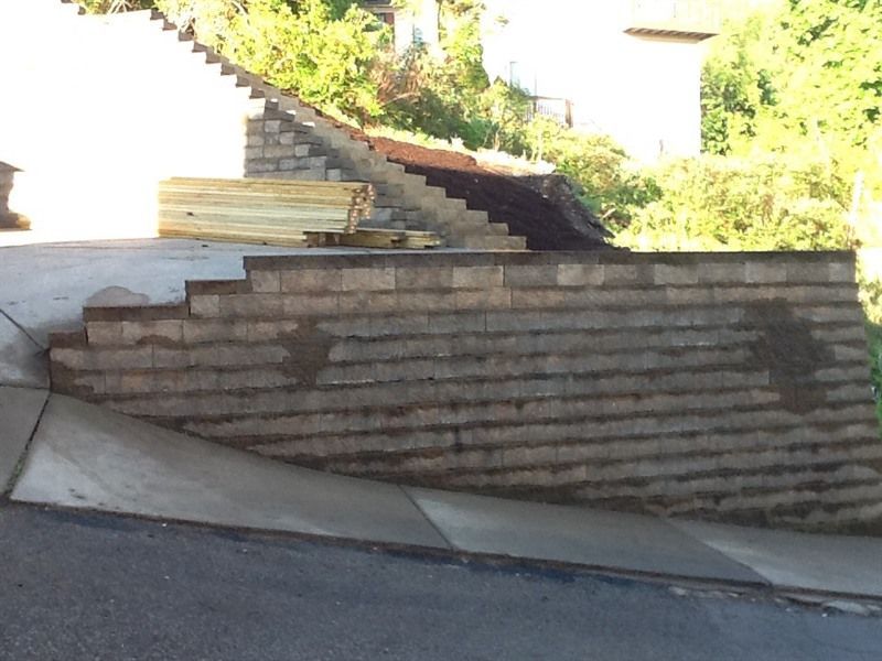 Stone retaining wall and stairs built into a hillside, with a driveway in the foreground.
