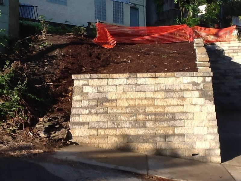 Stone retaining wall on a hillside with freshly laid mulch and orange safety netting.