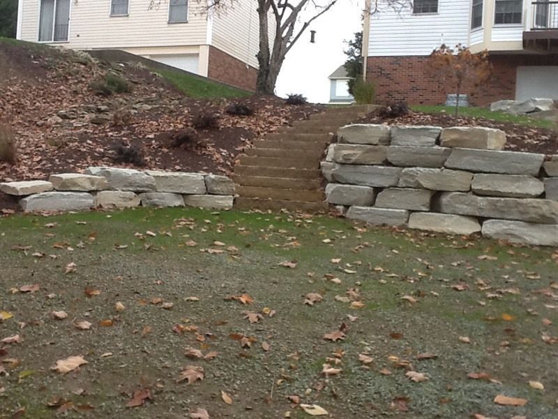 Stone retaining walls flank stone steps leading uphill; lawn in foreground with scattered leaves.