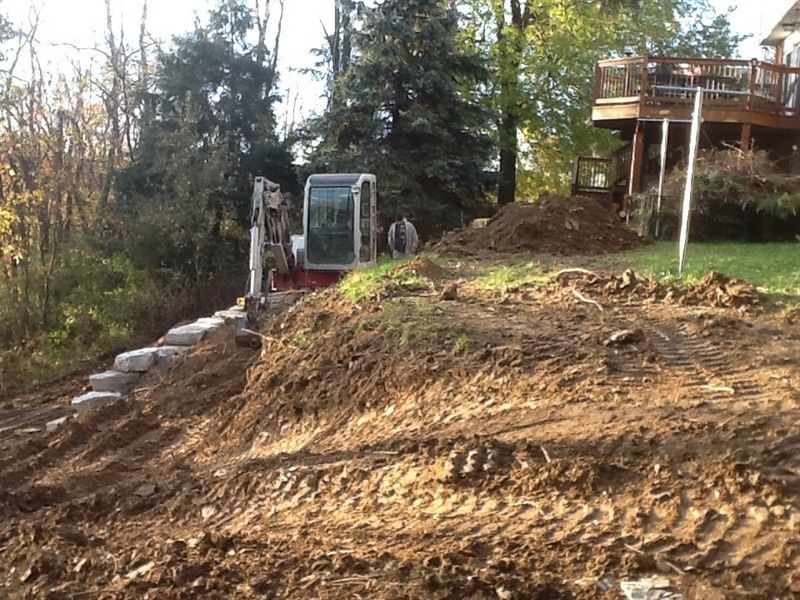 Construction site with an excavator building a stone retaining wall on a hillside.