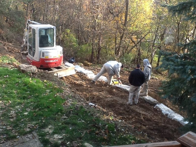 Construction workers building a retaining wall on a hillside with an excavator.