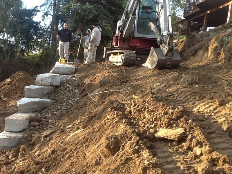Workers building stone steps on a hillside with an excavator.