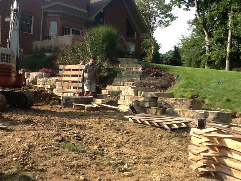 Construction worker standing near stone steps and retaining wall being built on a hillside.