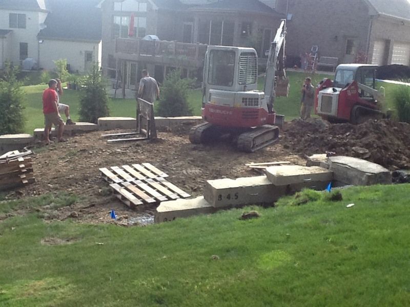 Construction site in backyard with mini excavator and workers moving materials.