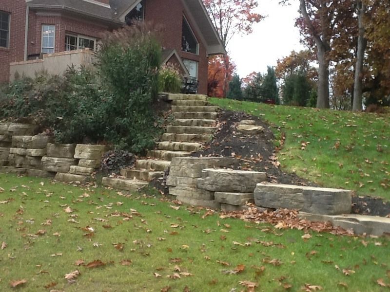 Stone steps leading up a grassy hill next to a house with fall foliage.