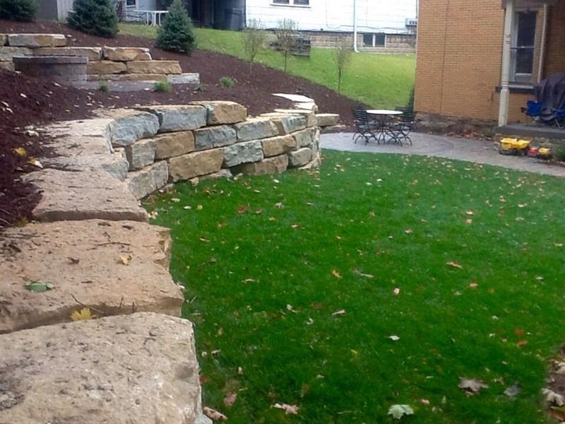 Stone retaining wall bordering a green lawn and patio area.