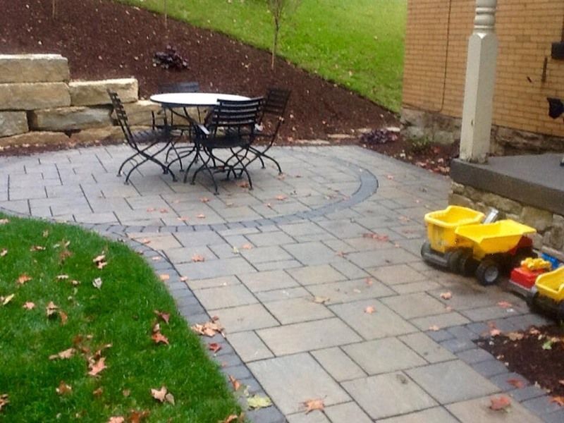 Stone patio with table and chairs, near a grassy area and building.