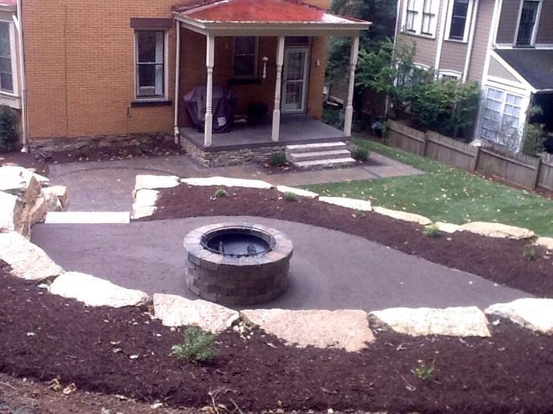 Backyard patio with fire pit, stone borders, and steps leading to a porch.