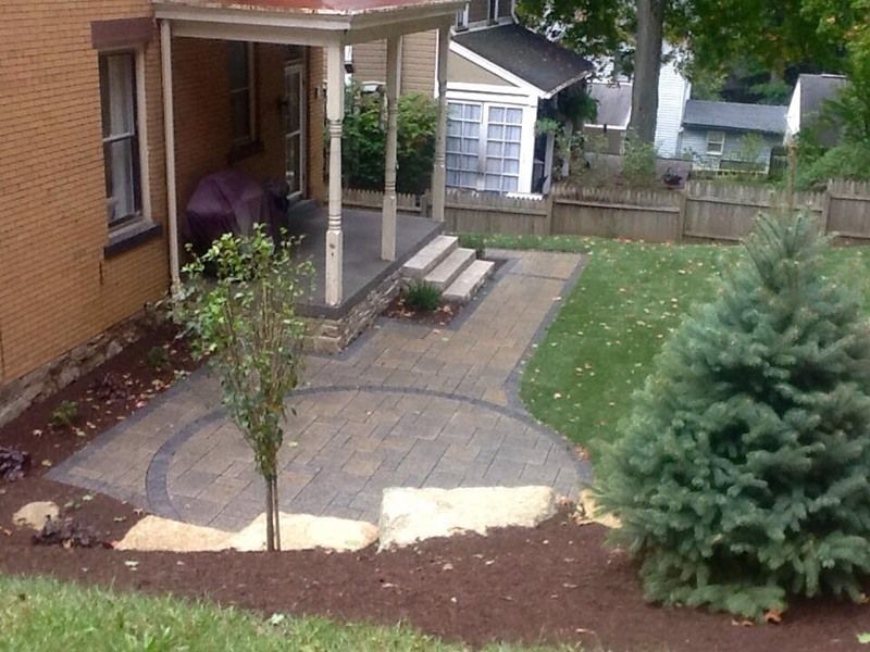Backyard patio with stamped concrete, a porch, trees, and landscaping.