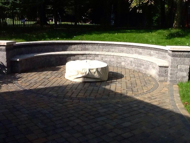 Circular brick patio with built-in seating, covered fire pit, and grassy lawn.