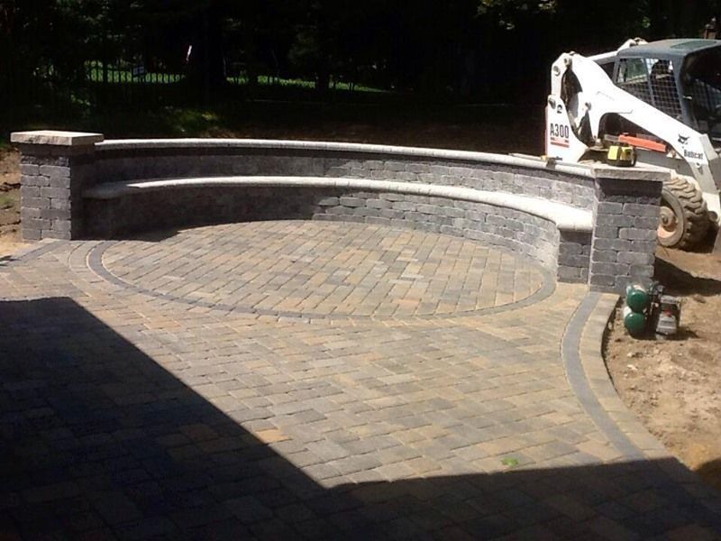 Brick patio with curved seating area and bobcat.
